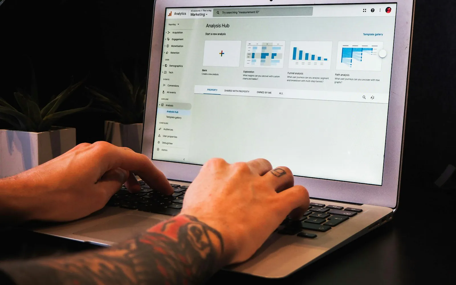 Hands typing on a laptop showing the Google Analytics 4 Analysis Hub with exploration, funnel and path analysis templates