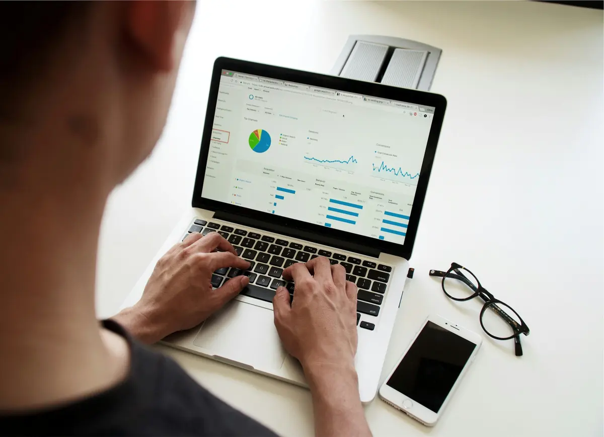 Over-the-shoulder view of a person typing on a laptop showing an analytics dashboard with pie and line charts